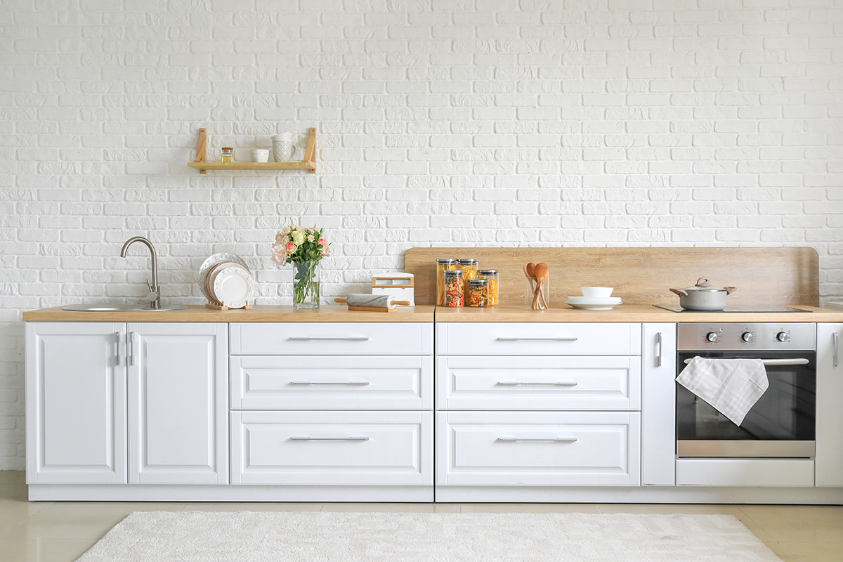 Cucina bianca moderna con piano lavoro legno e parete rivestita di mattoni bianchi.